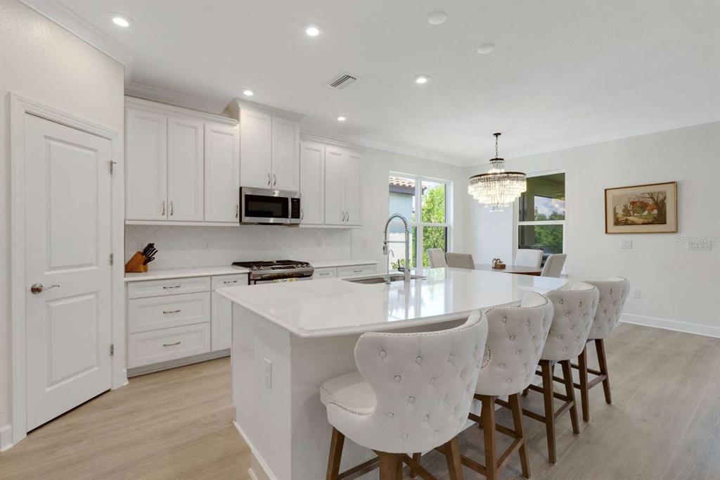 A white kitchen features a large island with bar seating, quartz countertops, and light flooring — 5410 MOREY FARMS LOOP, PALMETTO, FL