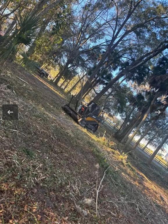 A John Deere forestry mulcher sits on a cleared, wooded lot with tall trees — 8549 S MAGNOLIA AVENUE, OCALA, FL