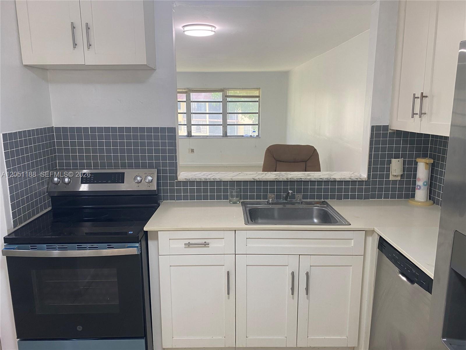 A kitchen features white cabinets, a black stove, a stainless steel sink, and gray tile — 1550 NE 191st St # 309, Miami FL 33179, MIAMI, FL