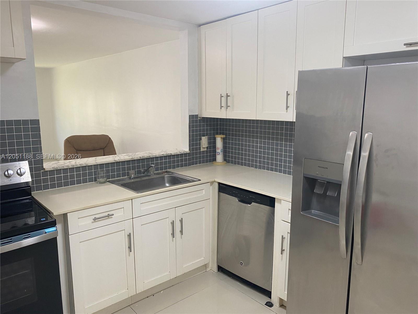 A kitchen features white cabinets, stainless steel appliances, a gray tiled backsplash, and a pass-through window — 1550 NE 191st St # 309, Miami FL 33179, MIAMI, FL