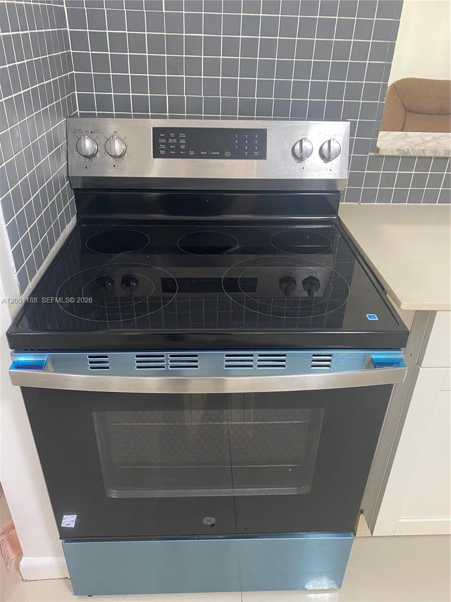 A stainless steel electric range with a glass cooktop sits against a tiled backsplash — 1550 NE 191st St # 309, Miami FL 33179, MIAMI, FL
