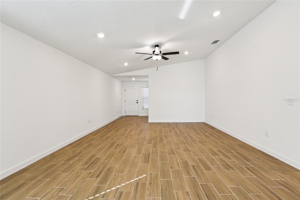 A bright, empty living room features white walls, a vaulted ceiling, and wood-look tile flooring — 5283 CAP ROAD, BROOKSVILLE, FL