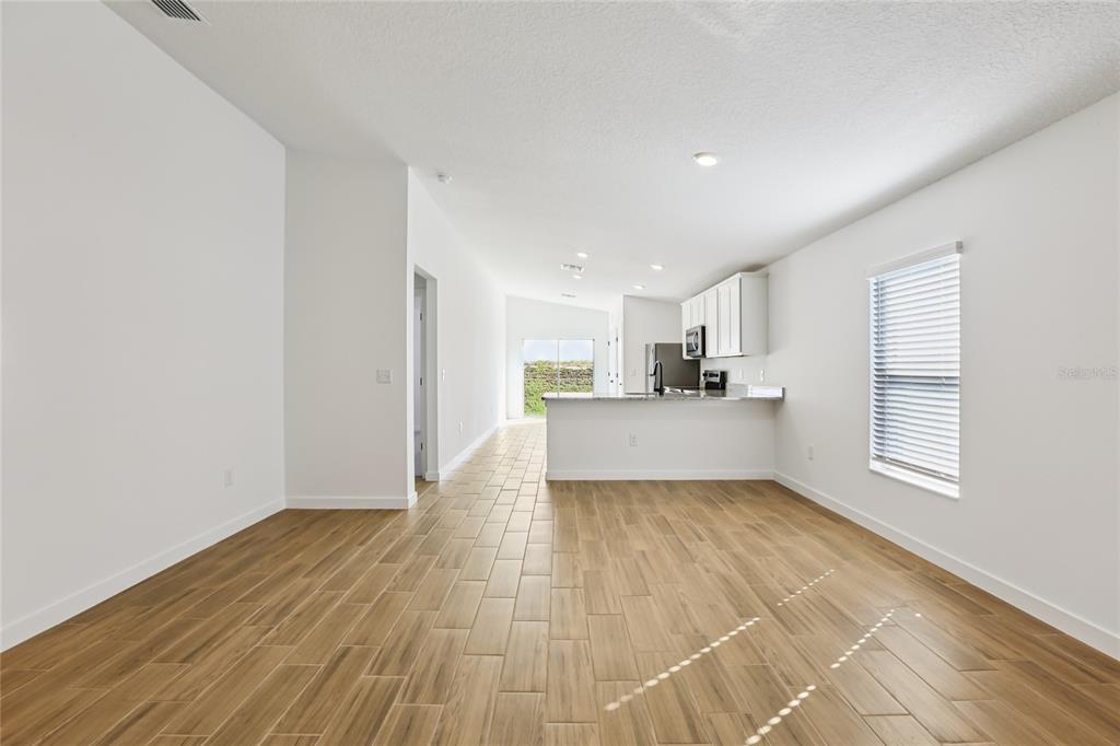 An open-concept living area features wood-look tile flooring, white walls, and a kitchen with cabinets — 5283 CAP ROAD, BROOKSVILLE, FL