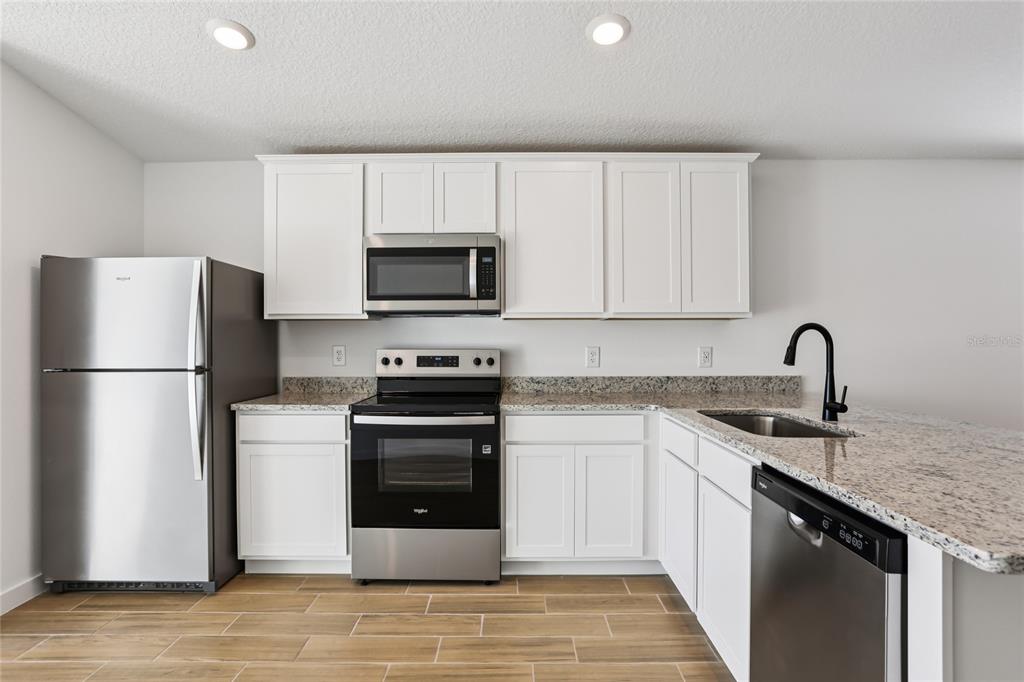 A kitchen features white cabinets, stainless steel appliances, granite countertops, and wood-look tile flooring — 5283 CAP ROAD, BROOKSVILLE, FL