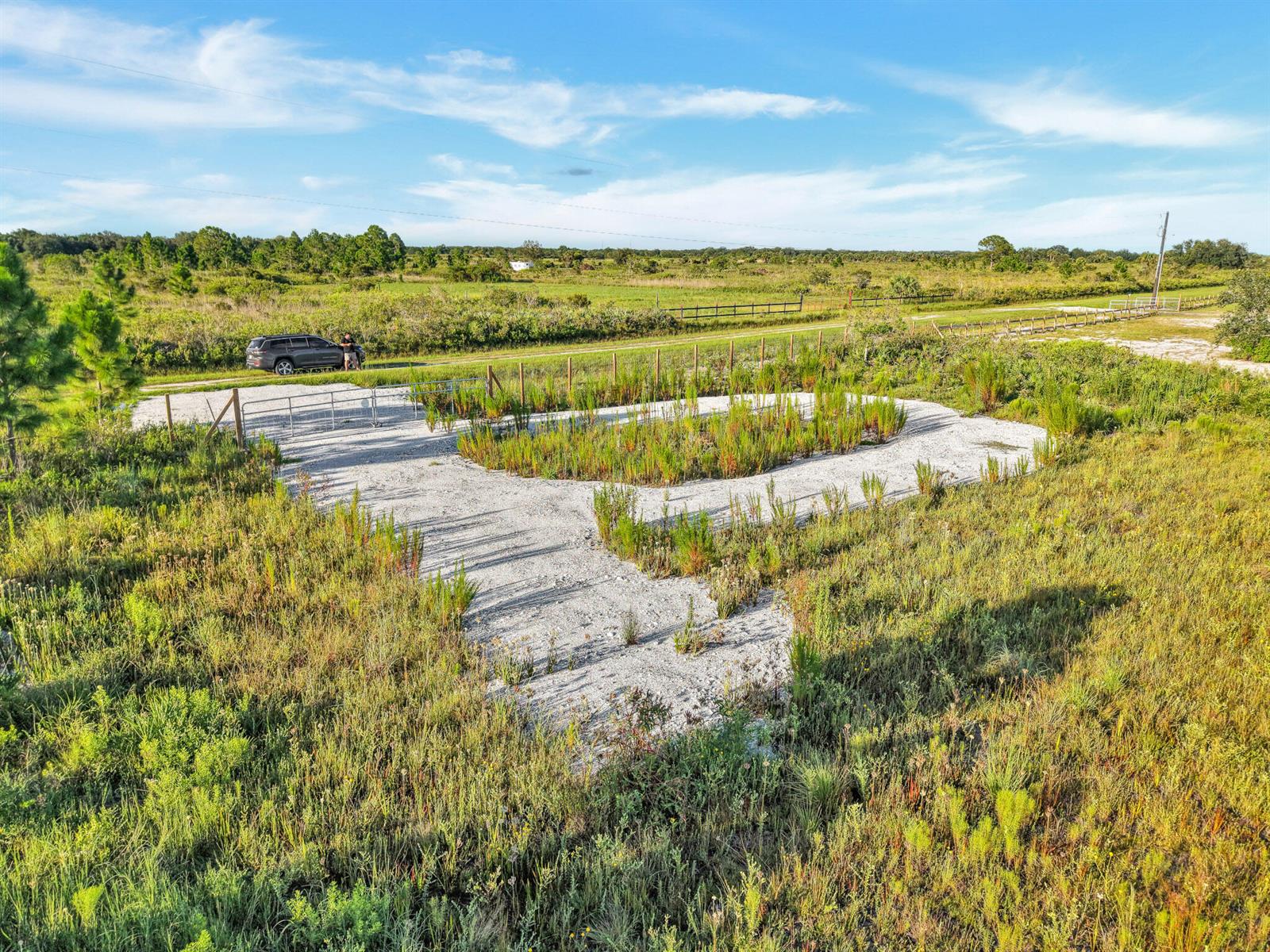 An aerial view shows a gravel driveway and parking area surrounded by open grassy fields — 22184 NW 278th Street, Okeechobee FL 34972, OKEECHOBEE, FL