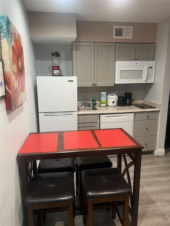 A small kitchen features gray cabinets, white appliances, a sink, and a dining table set — 3100 PARKWAY BOULEVARD UNIT 726, KISSIMMEE, FL