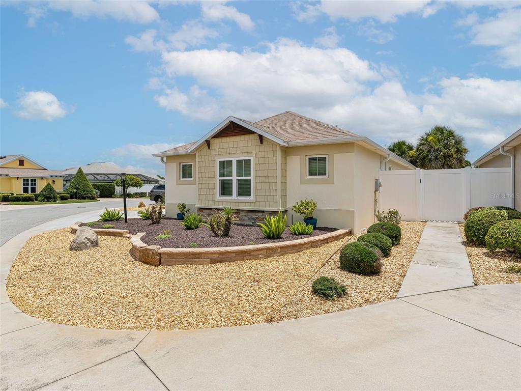 A single-story house with tan siding, a stone-accented garden bed, and a concrete driveway — 2877 FEUSTEL AVENUE, THE VILLAGES, FL