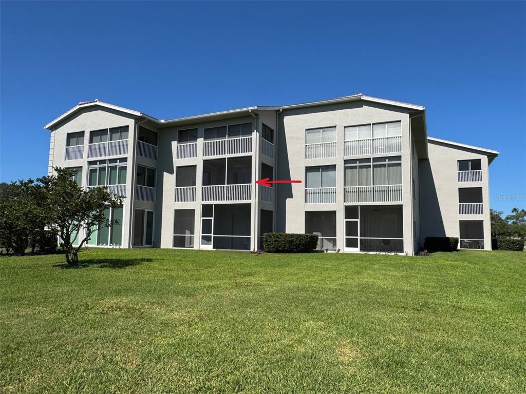A three-story apartment building features screened-in balconies with white railings and a grassy lawn — 9630 CLUB SOUTH CIRCLE UNIT 6209, SARASOTA, FL
