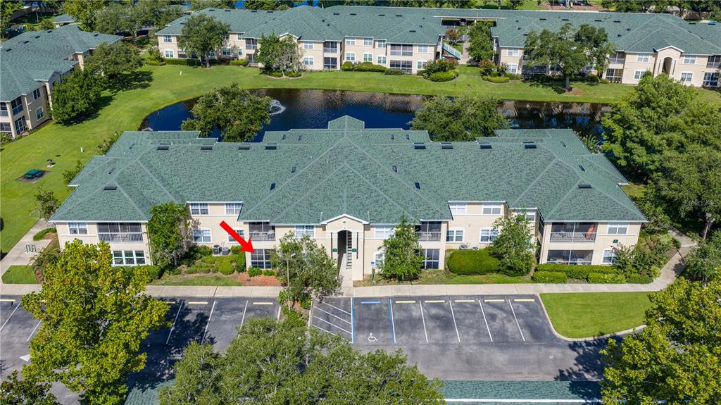 An aerial view shows a multi-story apartment building with a green roof near a pond — 830 AIRPORT ROAD UNIT 103, PORT ORANGE, FL