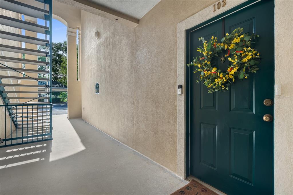 A dark green front door with a floral wreath sits beside an outdoor metal staircase — 830 AIRPORT ROAD UNIT 103, PORT ORANGE, FL