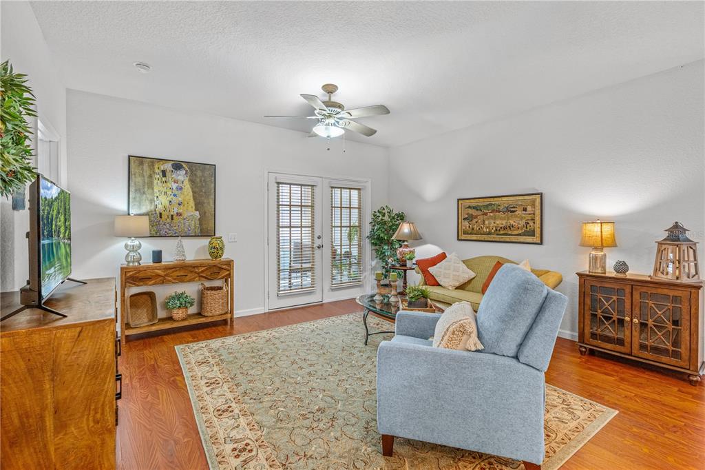 A living room features hardwood floors, a light blue armchair, a sofa, and French doors — 830 AIRPORT ROAD UNIT 103, PORT ORANGE, FL