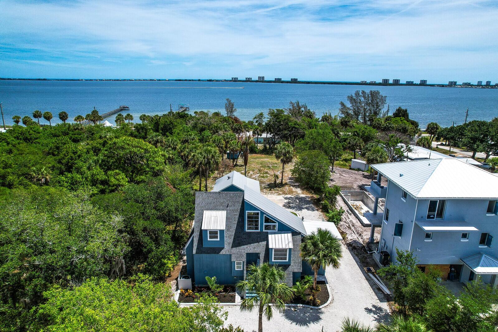 An aerial view shows a blue house with a gray roof near a large body water — 12000 Conklin Way, Jensen Beach FL 34957, JENSEN BEACH, FL