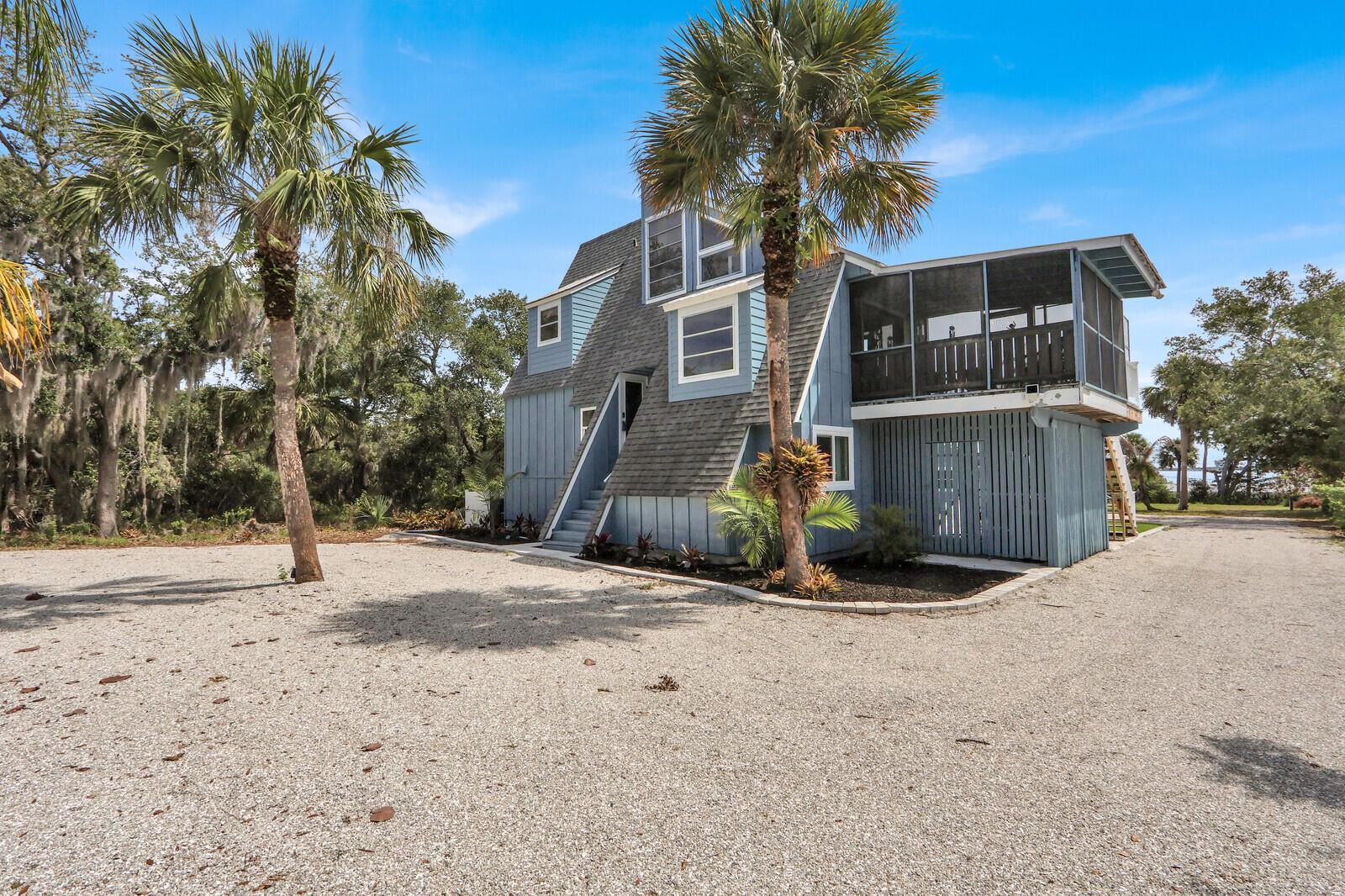 A blue, multi-story house with a screened-in porch stands on a large gravel lot — 12000 Conklin Way, Jensen Beach FL 34957, JENSEN BEACH, FL