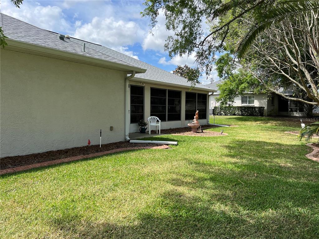 A view of a house exterior with a screened-in porch and a grassy backyard — 5333 NW 25TH LOOP, OCALA, FL