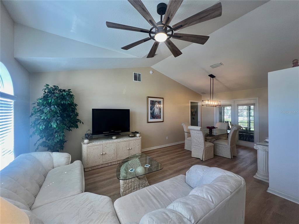 A living room and dining area feature vaulted ceilings, a ceiling fan, and wood-look flooring — 5333 NW 25TH LOOP, OCALA, FL