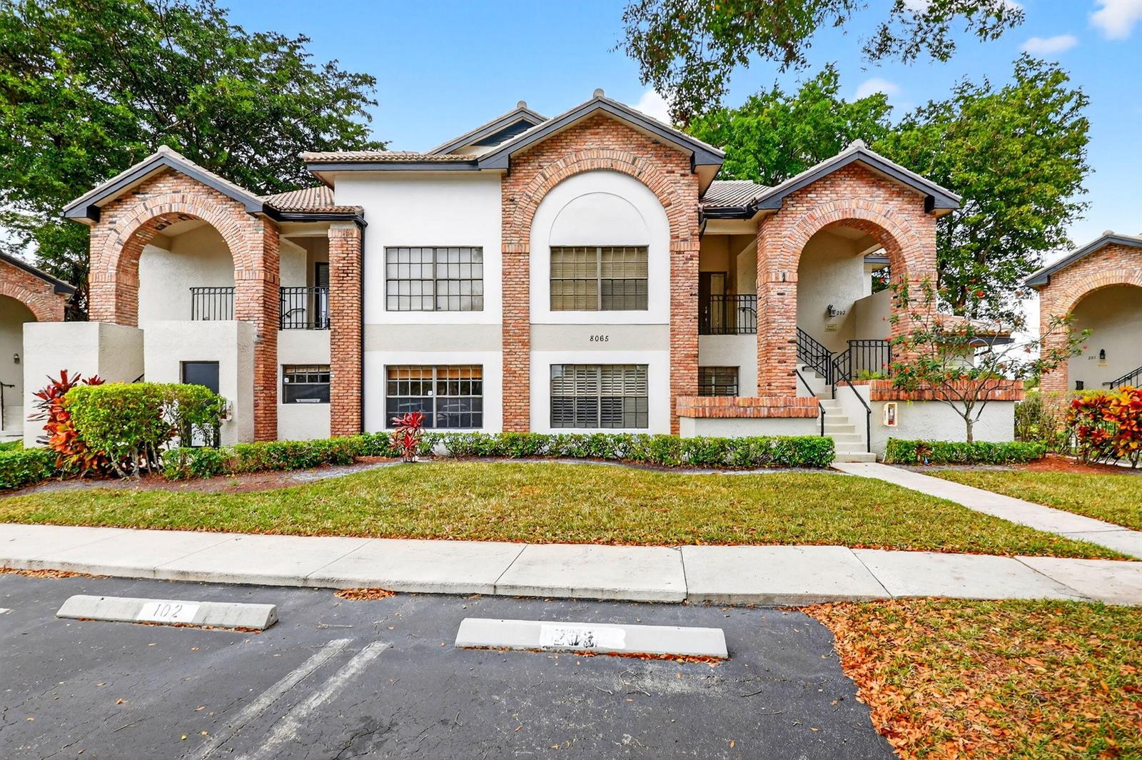 A two-story apartment building features brick arches, stucco walls, and a landscaped front lawn — 8065 Aberdeen Drive # 101, Boynton Beach FL 33472, BOYNTON BEACH, FL