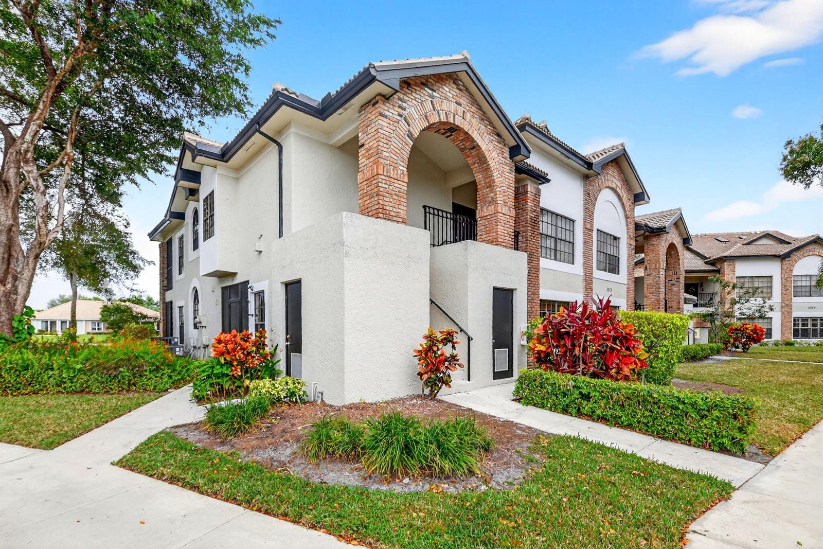 A two-story apartment building features stucco walls, brick arched entryways, and landscaped front gardens — 8065 Aberdeen Drive # 101, Boynton Beach FL 33472, BOYNTON BEACH, FL