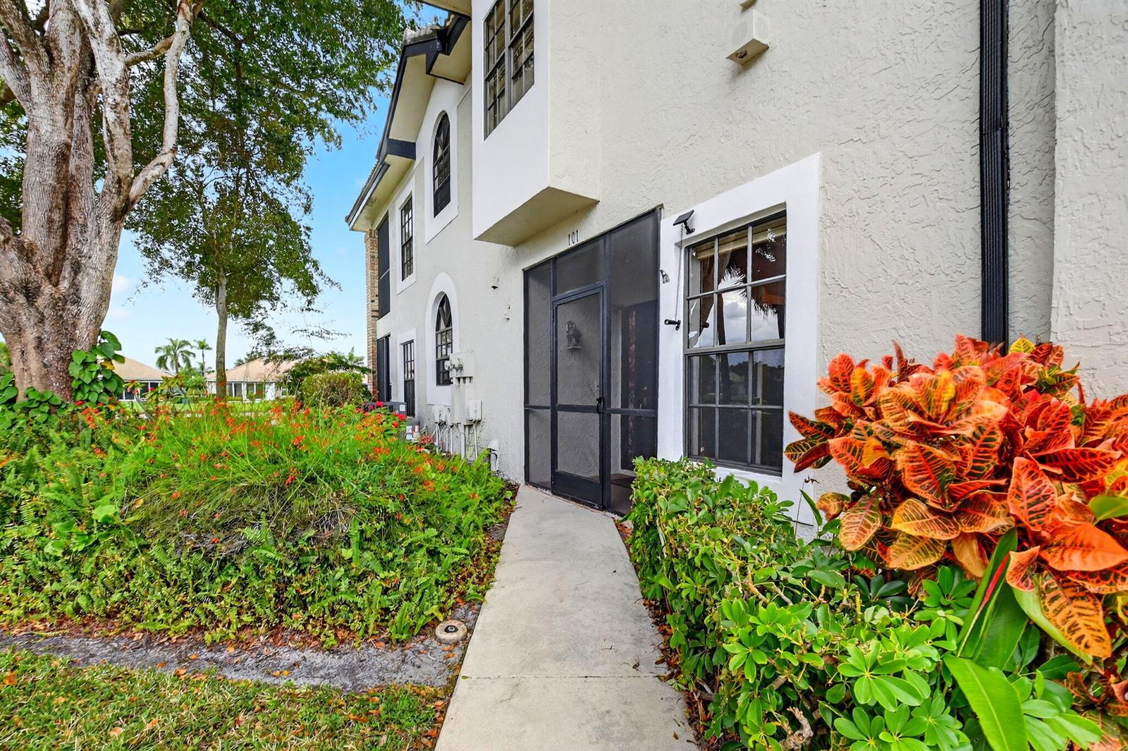 A concrete walkway leads to the screened front entrance of a two-story stucco building — 8065 Aberdeen Drive # 101, Boynton Beach FL 33472, BOYNTON BEACH, FL