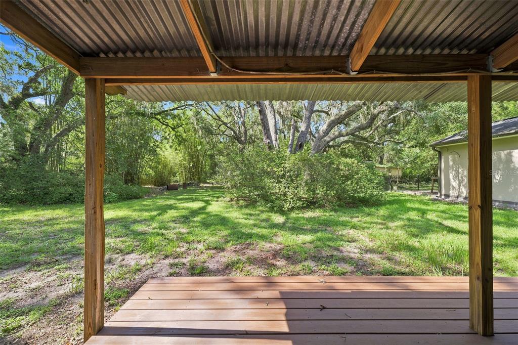 A covered wooden porch overlooks a grassy backyard with large trees and dense foliage — 16426 FORZANDO AVENUE, BROOKSVILLE, FL