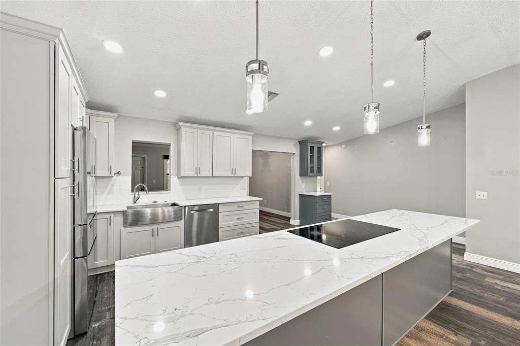 A modern kitchen features white cabinetry, a marble-topped island with a cooktop, and wood flooring — 16426 FORZANDO AVENUE, BROOKSVILLE, FL