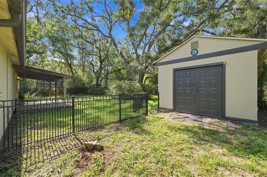 A backyard features a detached storage shed, a black metal fence, and a covered patio area — 16426 FORZANDO AVENUE, BROOKSVILLE, FL