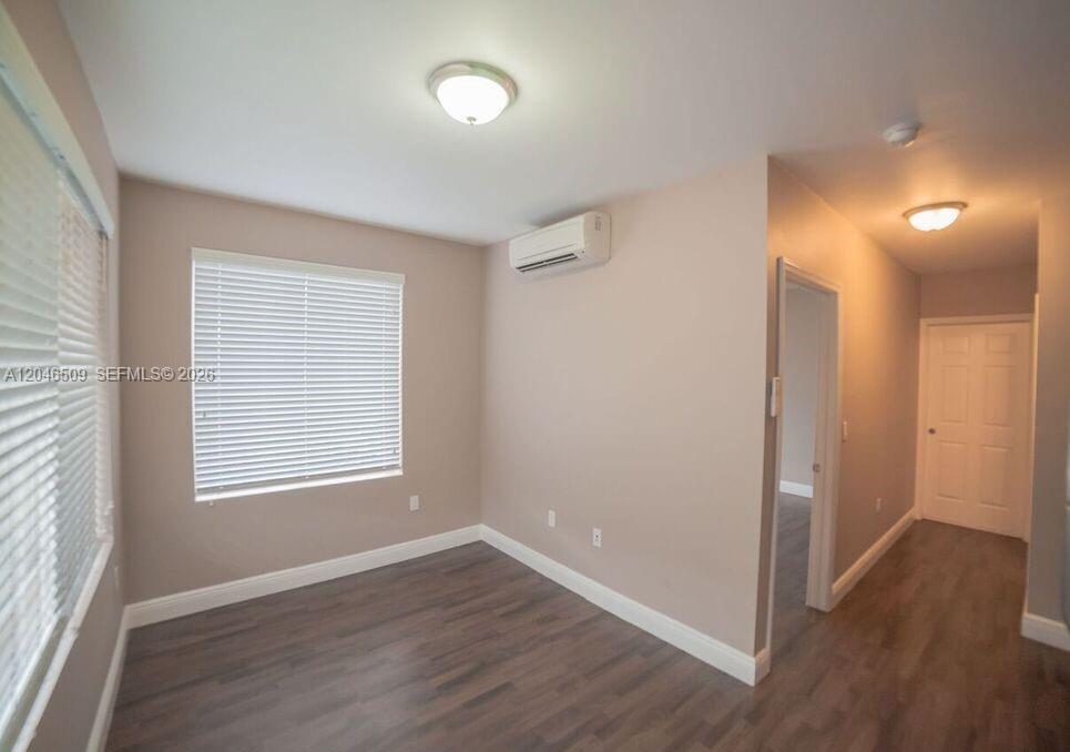 An empty room features dark wood-look flooring, light walls, a mini-split unit, and blinds — 1752 NW 1st St # 3, Miami FL 33125, MIAMI, FL