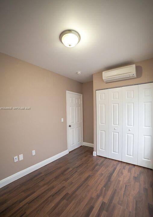 A bedroom with beige walls, wood-look flooring, a white door, and a wall-mounted air conditioner — 1752 NW 1st St # 3, Miami FL 33125, MIAMI, FL