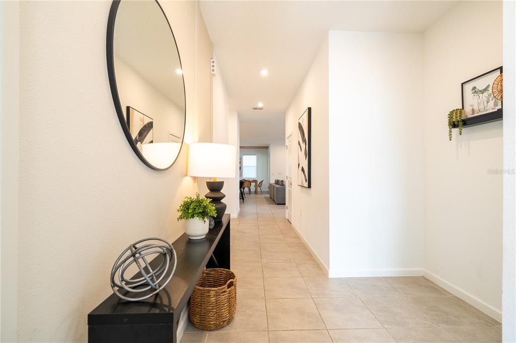A bright entryway features a black console table, a round mirror, and tile flooring — 2358 SALTY WINDS WAY, KISSIMMEE, FL