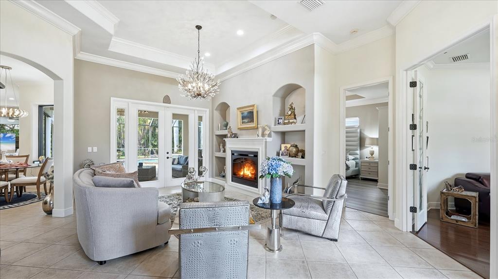A living room features a fireplace, built-in shelving, tile flooring, and a crystal chandelier — 3754 EAGLE HAMMOCK DRIVE, SARASOTA, FL