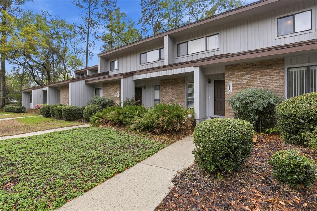 A two-story townhouse exterior features gray vertical siding, brick accents, and a concrete walkway — 3939 NW 29TH LANE, GAINESVILLE, FL