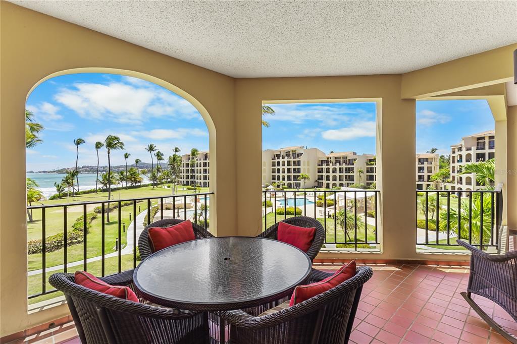 A covered balcony with a glass-top table, wicker chairs, and views of the ocean — 190 CANDELERO DR UNIT 228, HUMACAO, PR