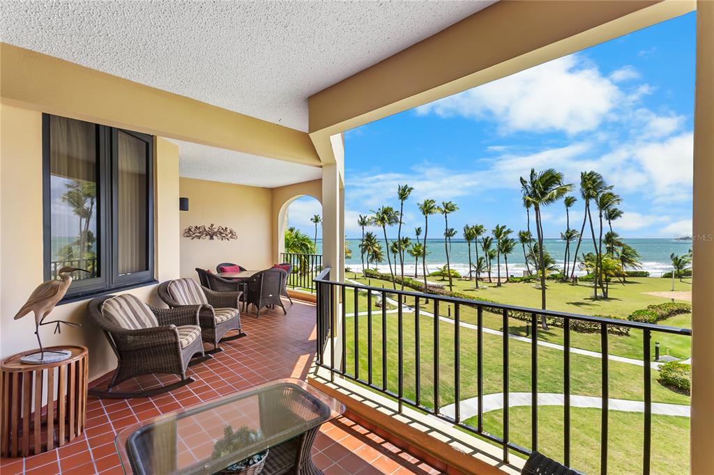 A tiled balcony with wicker furniture overlooks a grassy lawn and the ocean — 190 CANDELERO DR UNIT 228, HUMACAO, PR