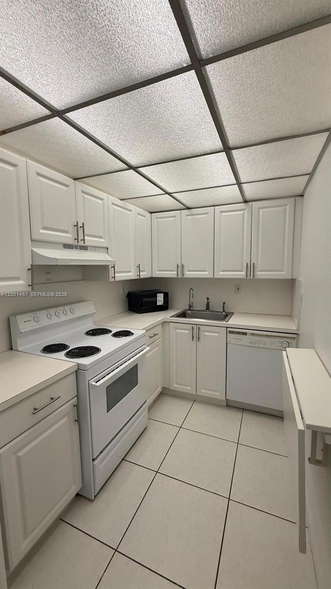 A galley kitchen features white cabinets, white appliances, and a drop ceiling with fluorescent lighting — 17530 NW 68th Ave # C3010, Hialeah FL 33015, HIALEAH, FL