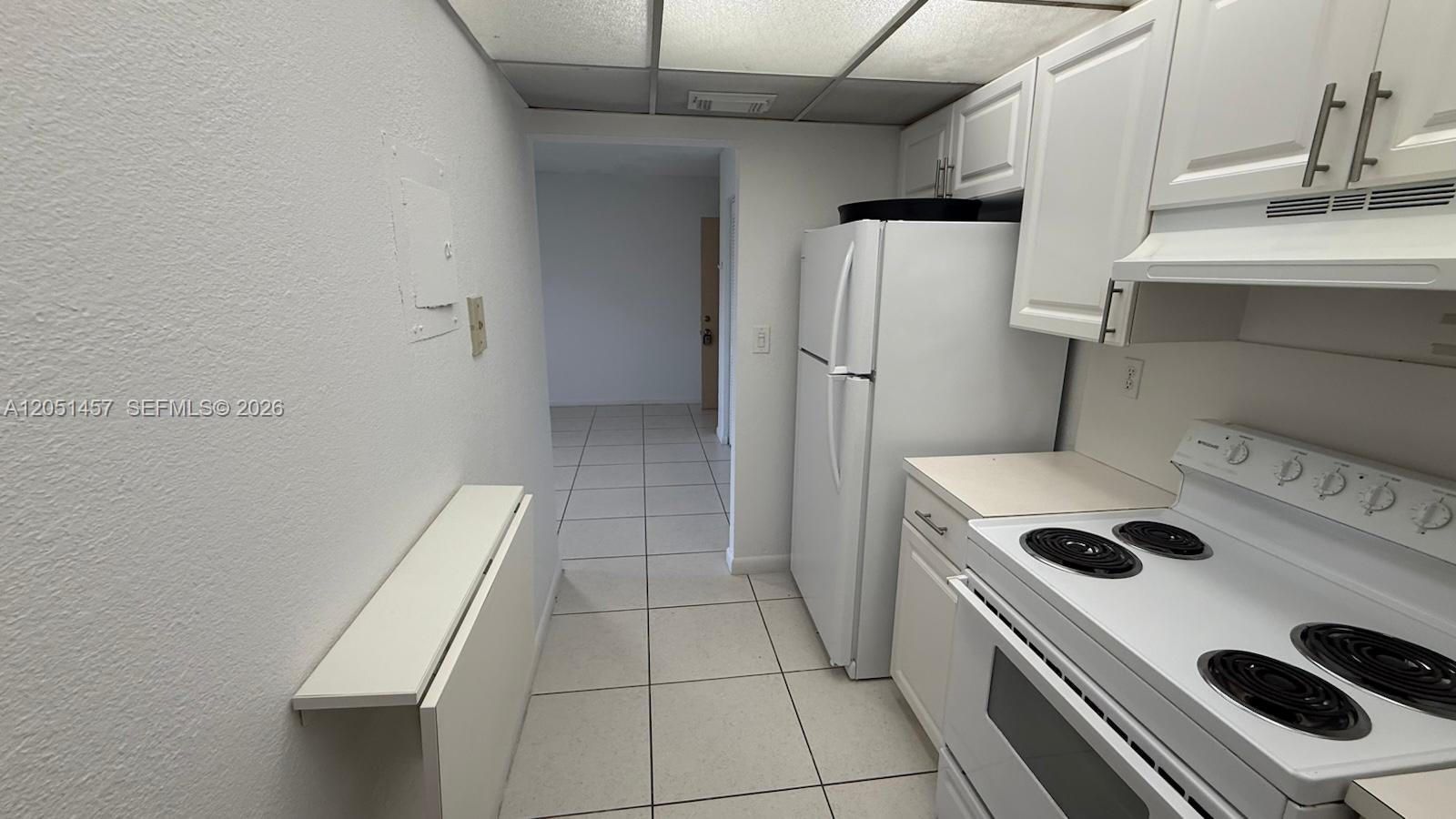 A galley kitchen features white cabinets, white appliances, and light-colored floor tiles — 17530 NW 68th Ave # C3010, Hialeah FL 33015, HIALEAH, FL