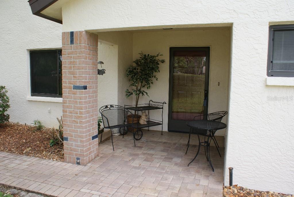 A covered patio features a brick pillar, a metal bench, a small table, and a door — 7445 CRESTWOOD DRIVE, WEEKI WACHEE, FL