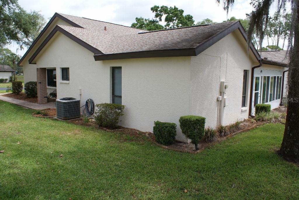 The exterior of a stucco house features a shingled roof, an air conditioning unit, and landscaping — 7445 CRESTWOOD DRIVE, WEEKI WACHEE, FL