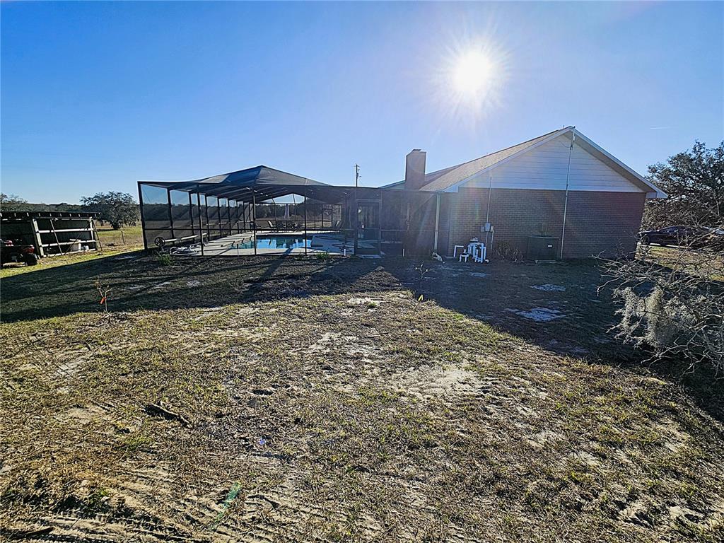 A brick house with a screened-in pool enclosure sits on a large, grassy lot — 13308 DUCK LAKE CANAL ROAD, DADE CITY, FL