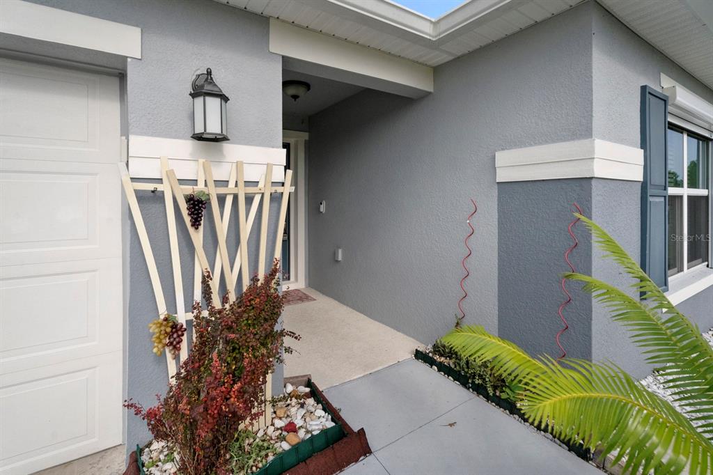 A gray house exterior features a covered entryway, a wooden trellis, and a small garden — 4521 CASABLANCA AVENUE, KISSIMMEE, FL