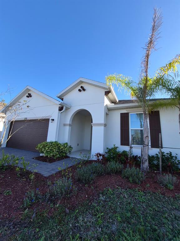 A single-story house exterior with a brown garage door, arched entryway, and a palm tree — 1772 STAMEN DRIVE, KISSIMMEE, FL
