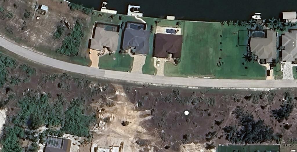 This aerial view shows a vacant lot across the street from several waterfront residential homes — 15061 TAURUS CIRCLE, PORT CHARLOTTE, FL