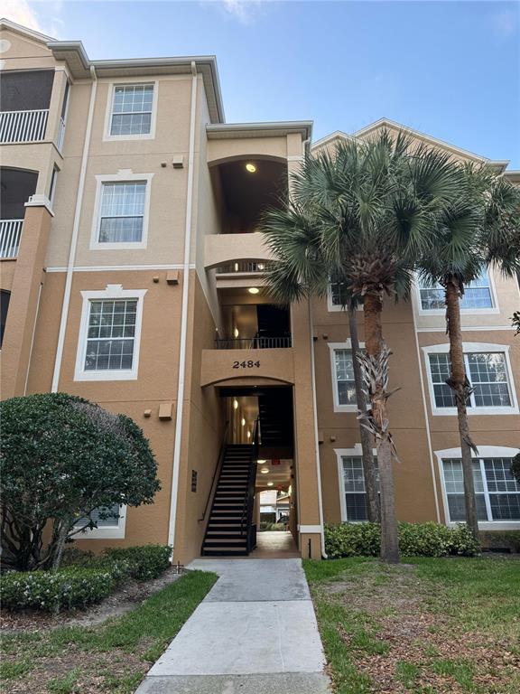 A three-story apartment building exterior features tan stucco walls, white trim, and a central staircase — 2484 SAN TECLA STREET UNIT 402, ORLANDO, FL