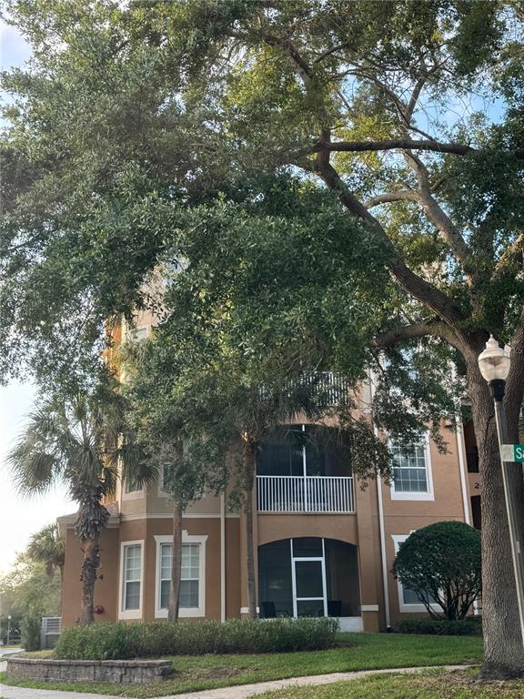 A multi-story apartment building features tan stucco walls, screened balconies, and mature oak trees — 2484 SAN TECLA STREET UNIT 402, ORLANDO, FL