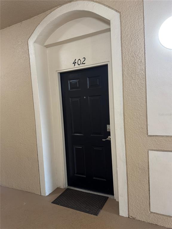 A black apartment door labeled 402 is set within a beige arched entryway — 2484 SAN TECLA STREET UNIT 402, ORLANDO, FL