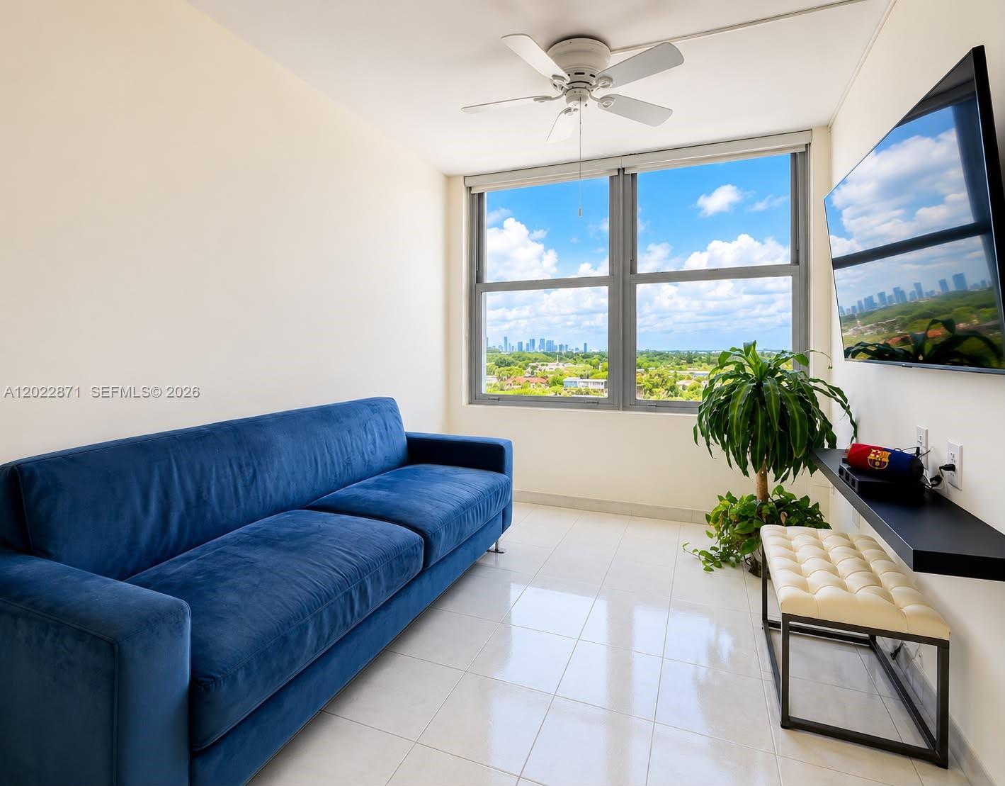 A living room features a blue sofa, a wall-mounted television, and a window with city views — 2899 Collins Ave # 1042, Miami Beach FL 33140, MIAMI BEACH, FL