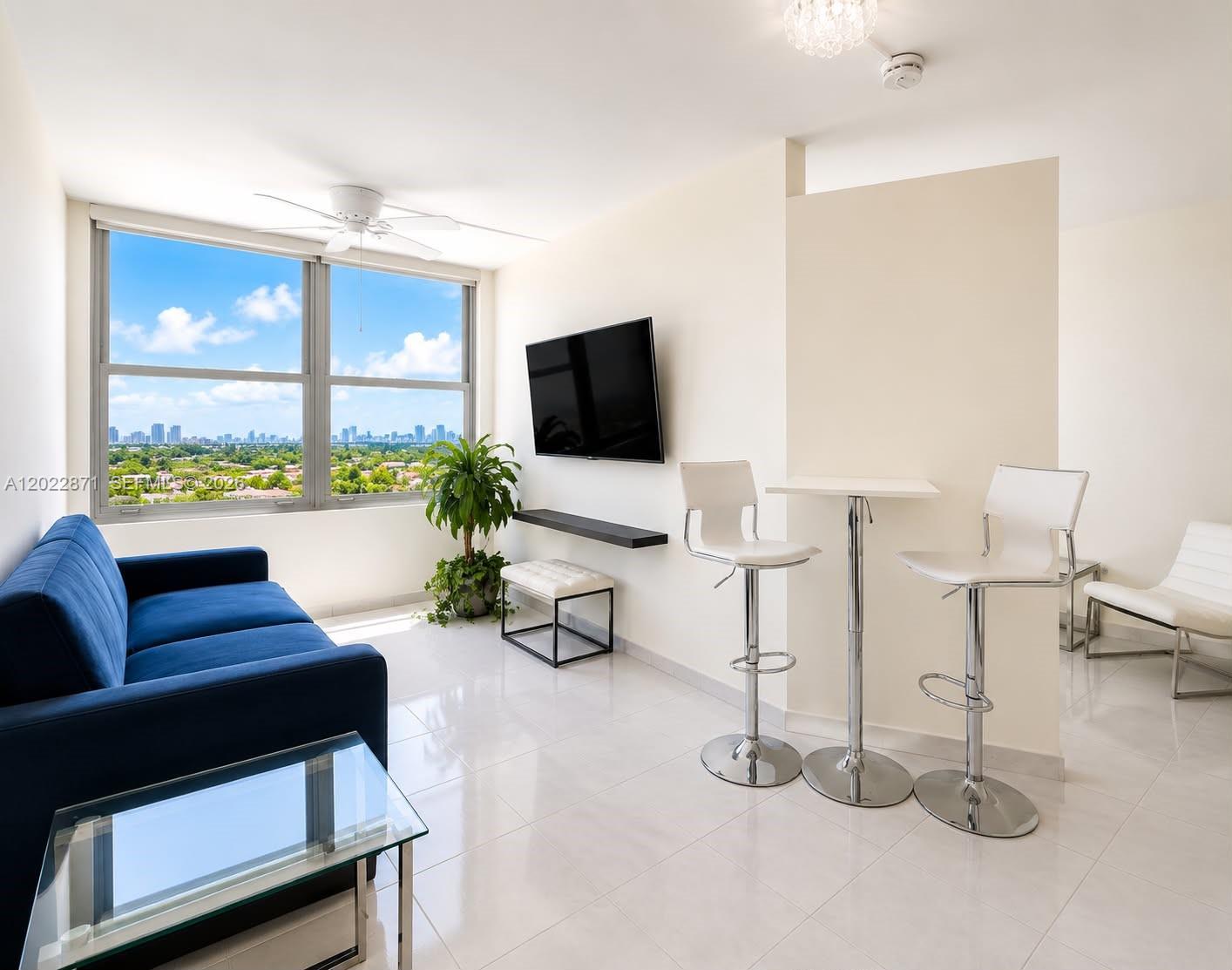 A living room features a blue sofa, a wall-mounted television, and a high-top dining table — 2899 Collins Ave # 1042, Miami Beach FL 33140, MIAMI BEACH, FL