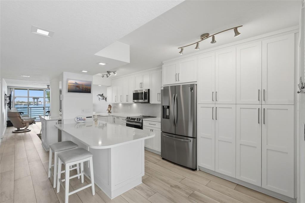 A modern white kitchen features stainless steel appliances, a quartz island, and views of water — 6081 BAHIA DEL MAR CIRCLE UNIT 251, ST PETERSBURG, FL