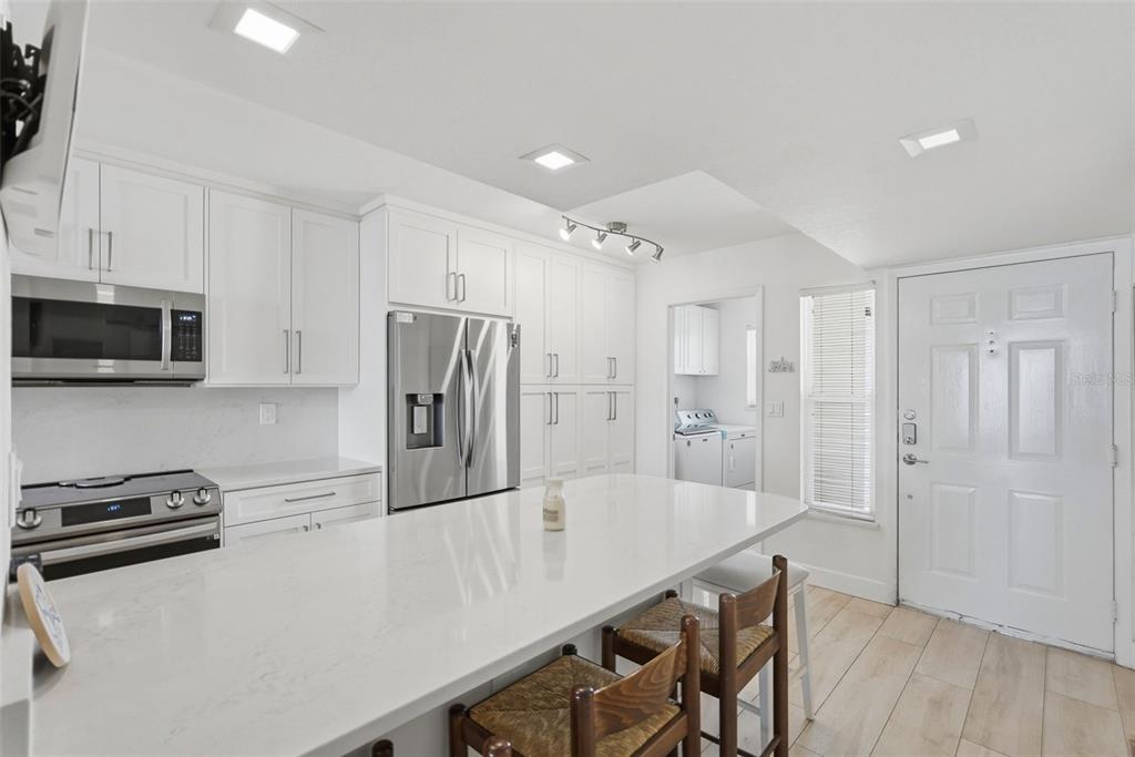 A modern kitchen features white cabinetry, a large quartz island, stainless steel appliances, and wood flooring — 6081 BAHIA DEL MAR CIRCLE UNIT 251, ST PETERSBURG, FL