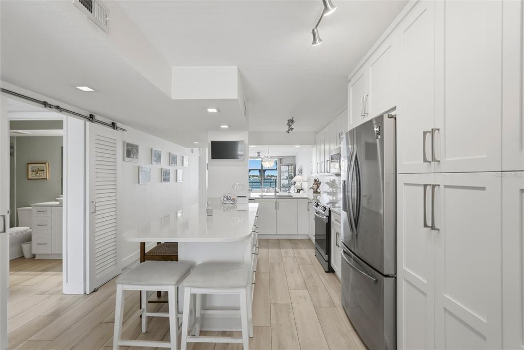 A modern kitchen features white cabinetry, a quartz island with bar seating, and stainless appliances — 6081 BAHIA DEL MAR CIRCLE UNIT 251, ST PETERSBURG, FL