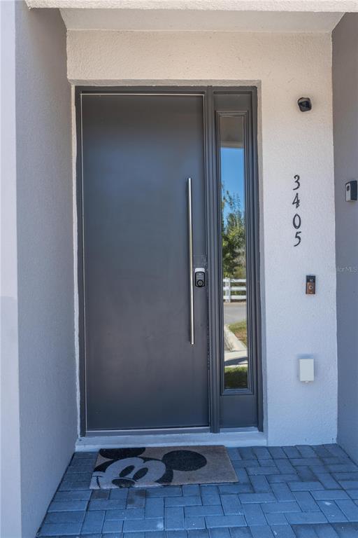 A modern dark gray front door with a vertical handle and a side window panel — 3405 TRANQUIL TRAIL, KISSIMMEE, FL