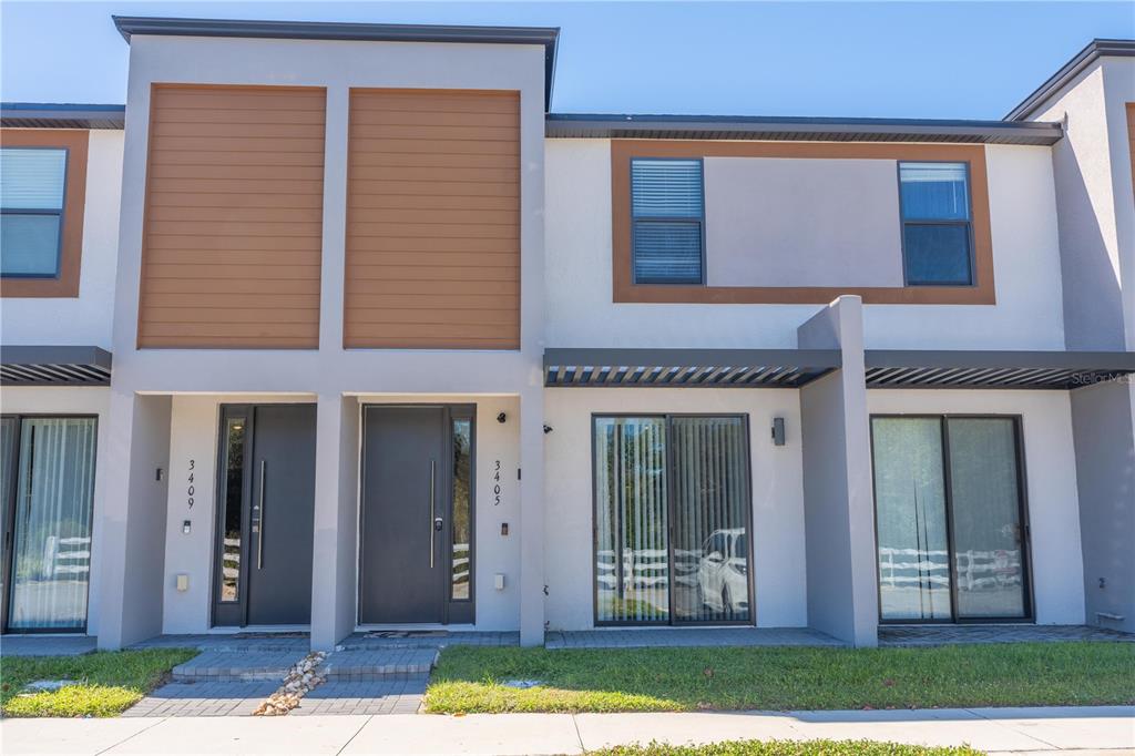 A modern two-story townhouse exterior features a mix of wood-look siding, stucco, and glass doors — 3405 TRANQUIL TRAIL, KISSIMMEE, FL